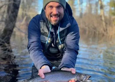 An excited fisherman wading in Sebago Lake, showing off his catch