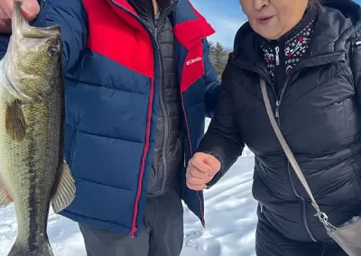 A young man and older woman in winter gear smiling with the young man holding the large mouth bass they caught