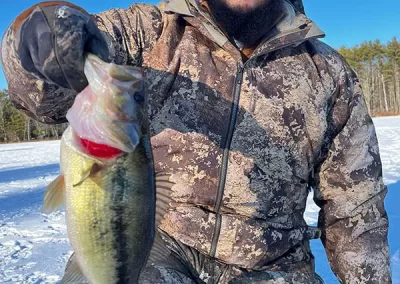 A young man in winter gear kneeling on the ice, showing off his catch