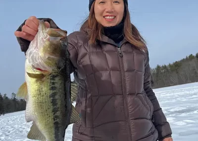 A woman in winter gear with a snowy background holding her fish